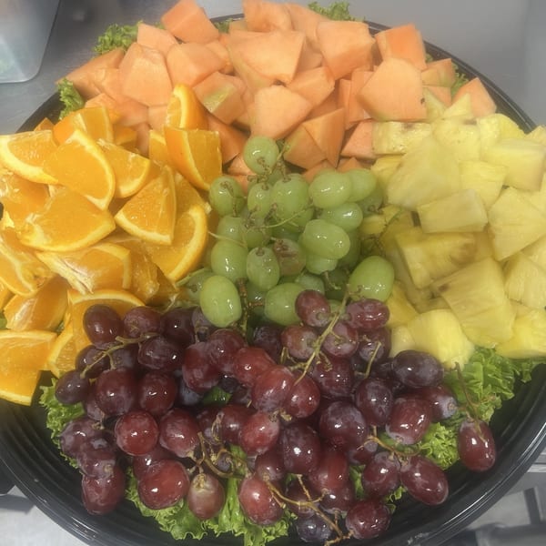 A platter of fresh fruit including cantaloupe, oranges, green grapes, red grapes, and pineapple.