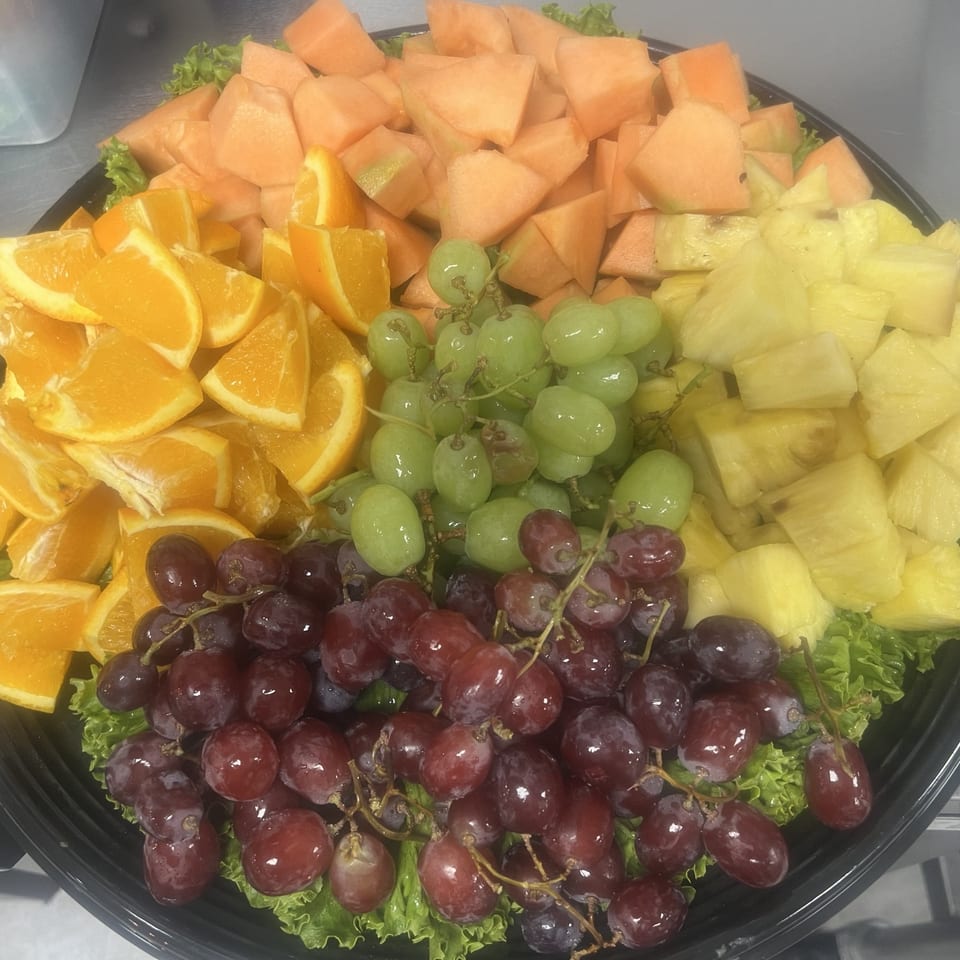 A platter of fresh fruit including cantaloupe, oranges, green grapes, red grapes, and pineapple.