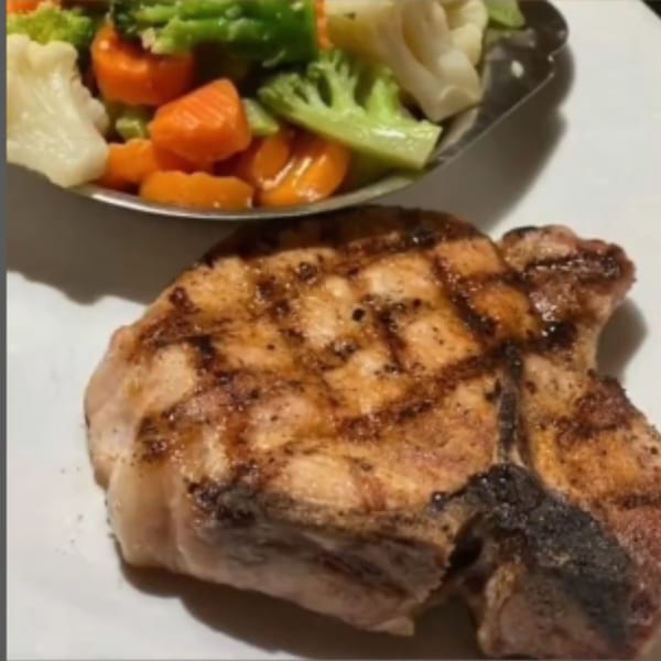 Grilled pork chop with char marks, served alongside a medley of steamed vegetables.