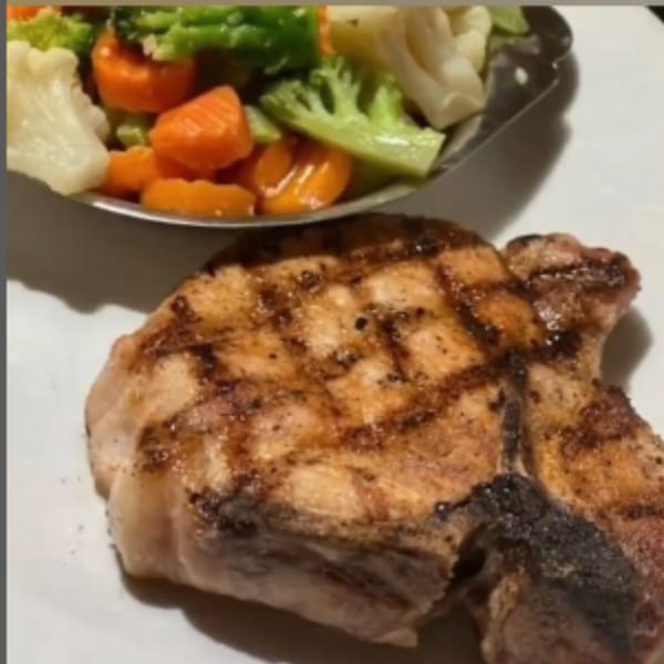 Grilled pork chop with grill marks, served with a side of steamed carrots, broccoli, and cauliflower.