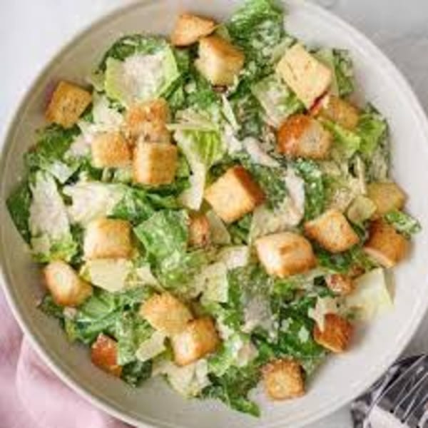 Overhead view of a Caesar salad with romaine lettuce, croutons, and parmesan cheese in a white bowl.