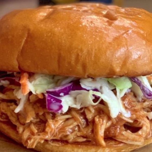 Close-up of a pulled pork sandwich on a brioche bun, topped with colorful coleslaw.