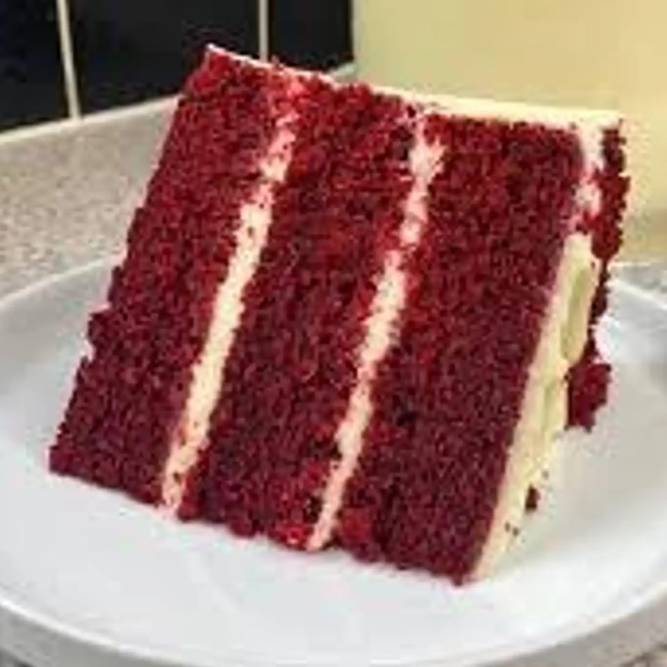 A slice of Grille No. 13's red velvet cake with white cream cheese frosting layers on a white plate.