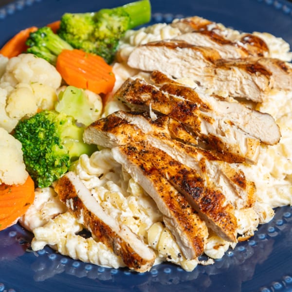 Grilled chicken slices over creamy pasta with a side of steamed broccoli, cauliflower, and carrots.