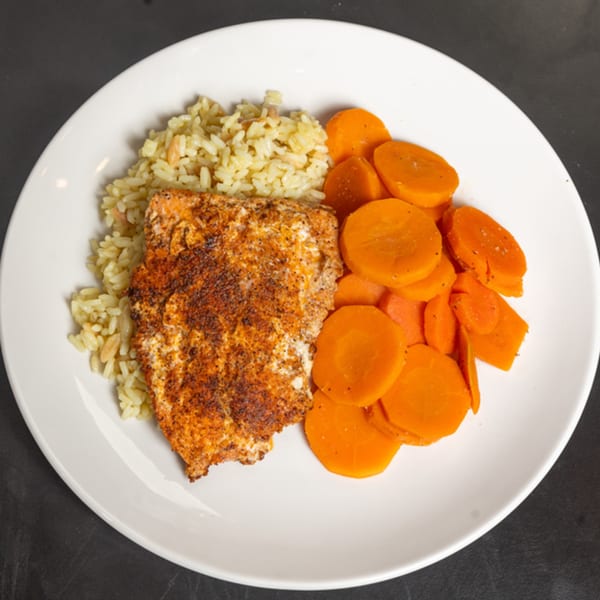 Seasoned fish fillet with rice pilaf and sliced carrots on a white plate.